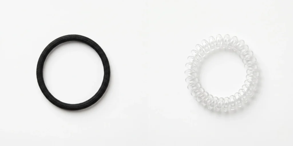 Standard black rubber elastic hair tie and clear spiral coil hair tie displayed side by side for breakage comparison